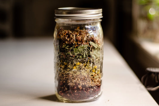 Herbal oxymel, wildcrafted herbs, and vintage apothecary jar on rustic table.